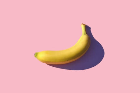 A single banana against the pink backdrop