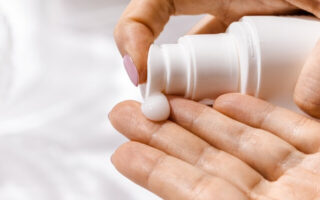 A close-up of a hand squeezing moisturizer out of a bottle, displaying the smooth and creamy texture of the product