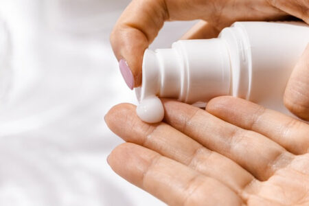 A close-up of a hand squeezing moisturizer out of a bottle, displaying the smooth and creamy texture of the product