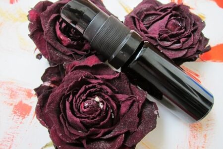 A black colored vitamin C serum bottle placed between dark red roses