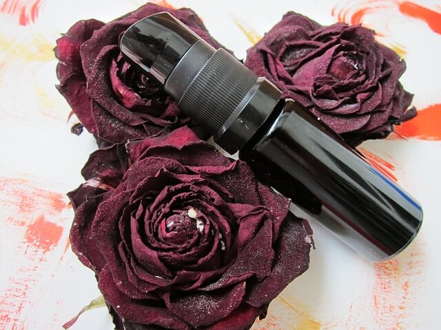 A black colored vitamin C serum bottle placed between dark red roses